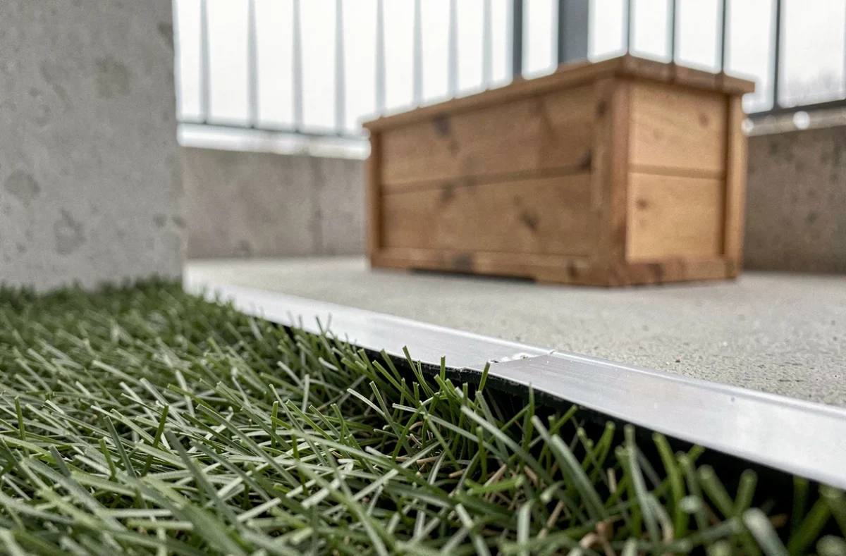 Détail d'un bord de gazon synthétique mal fixé sur un balcon, illustration d'une erreur courante d'installation